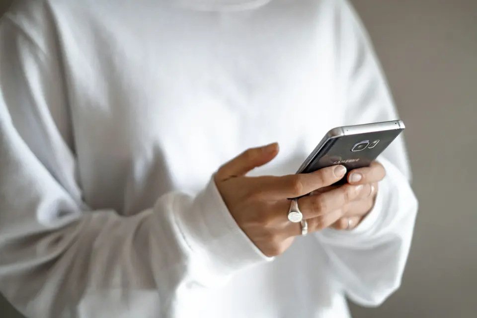 Person i hvit genser som bruker en mobiltelefon med begge hender